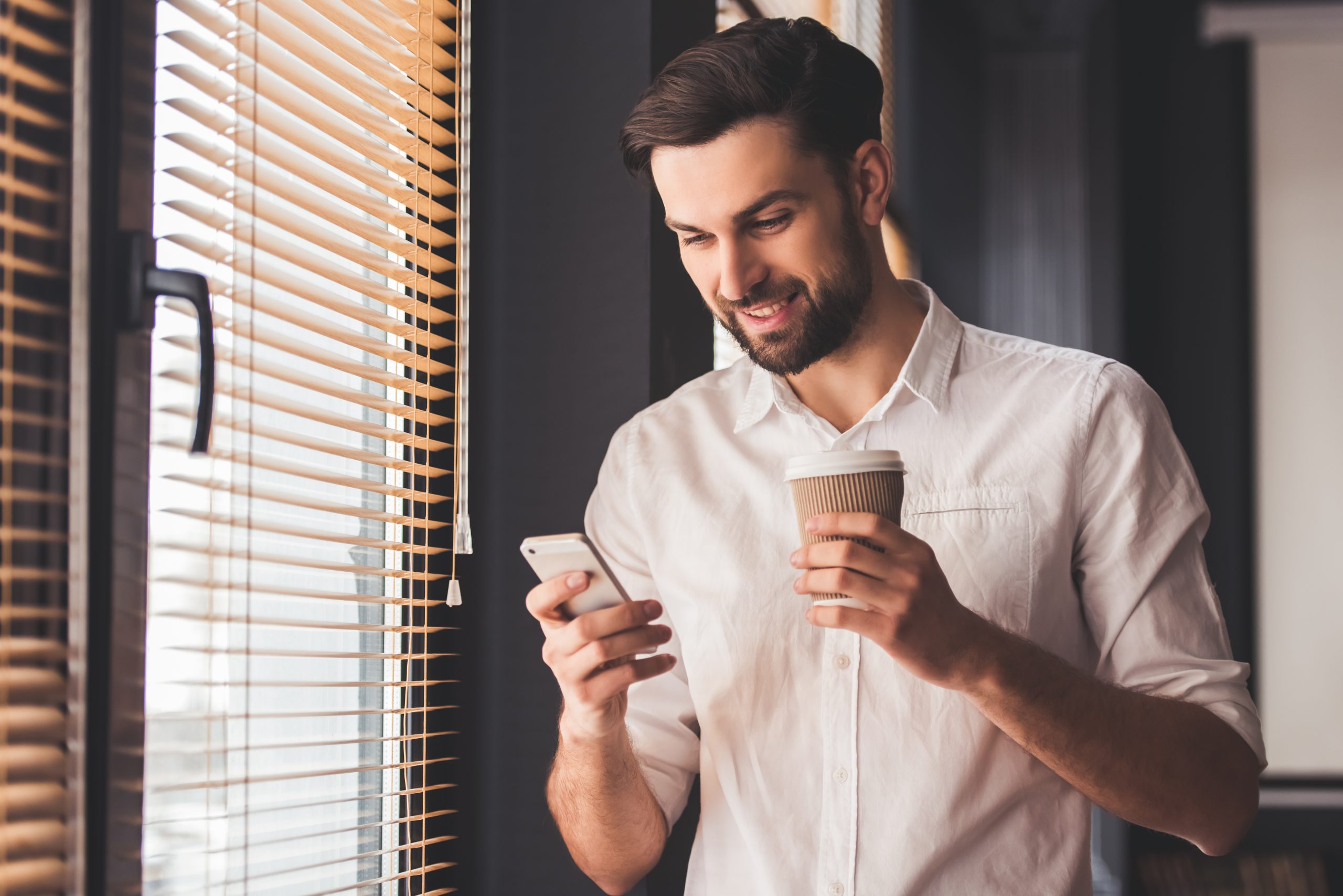 Homem branco usando uma plataforma de gamificação no smartphone enquanto segura um copo da café.
